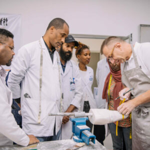 Human Study trainer at a workbench demonstrating work with plaster positive model to a group of students standing around him