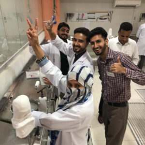 students standing at a workbench looking at the camera, smiling and showing thumbs up